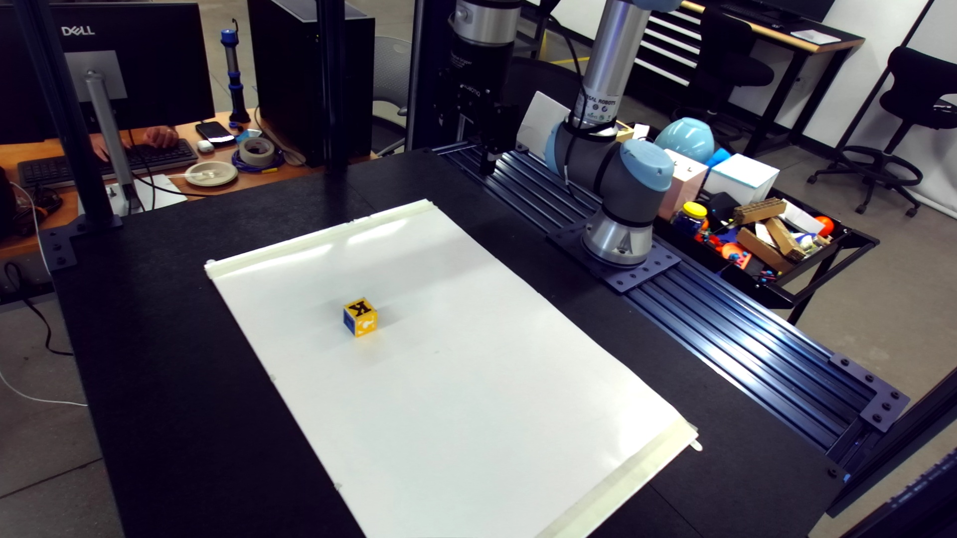 A yellow letter cube on a white work surface beside a robot arm.